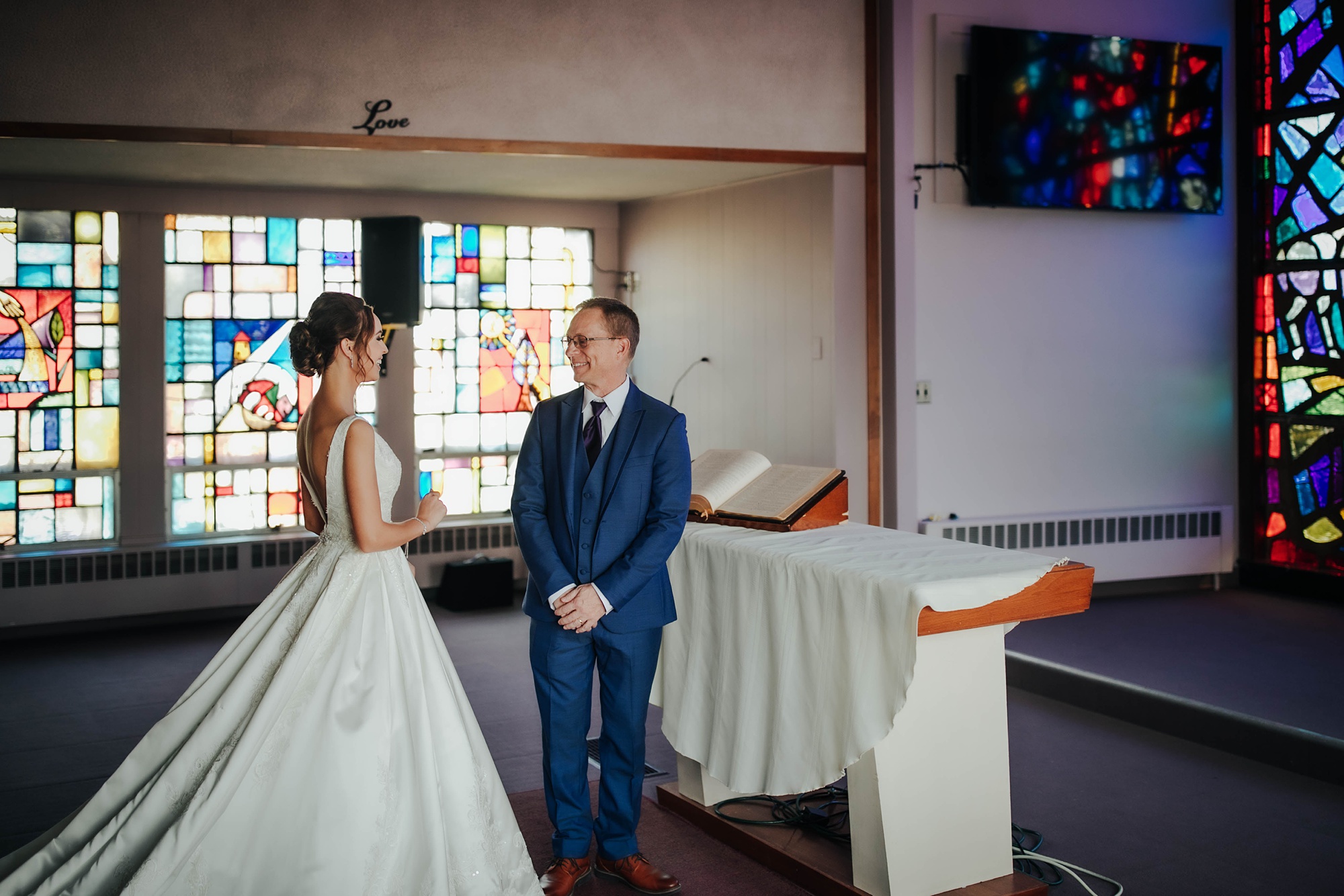 bride and father have first look in church by stained glass window