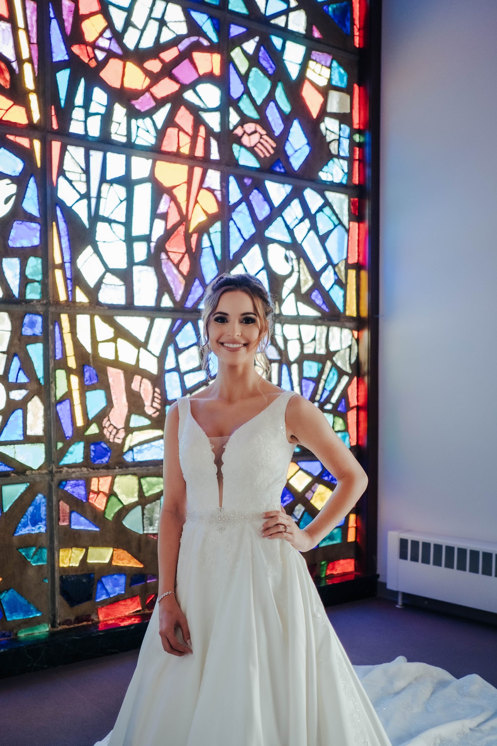 bride poses with hands on her hips in front of stained glass window in Ohio church