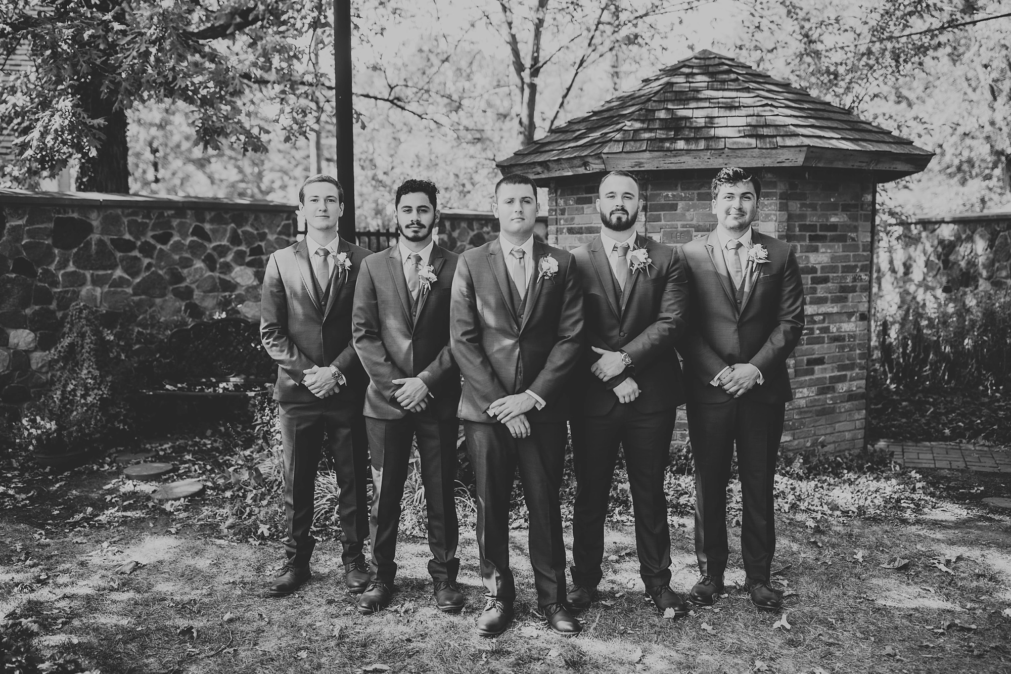groom poses with four groomsmen in garden