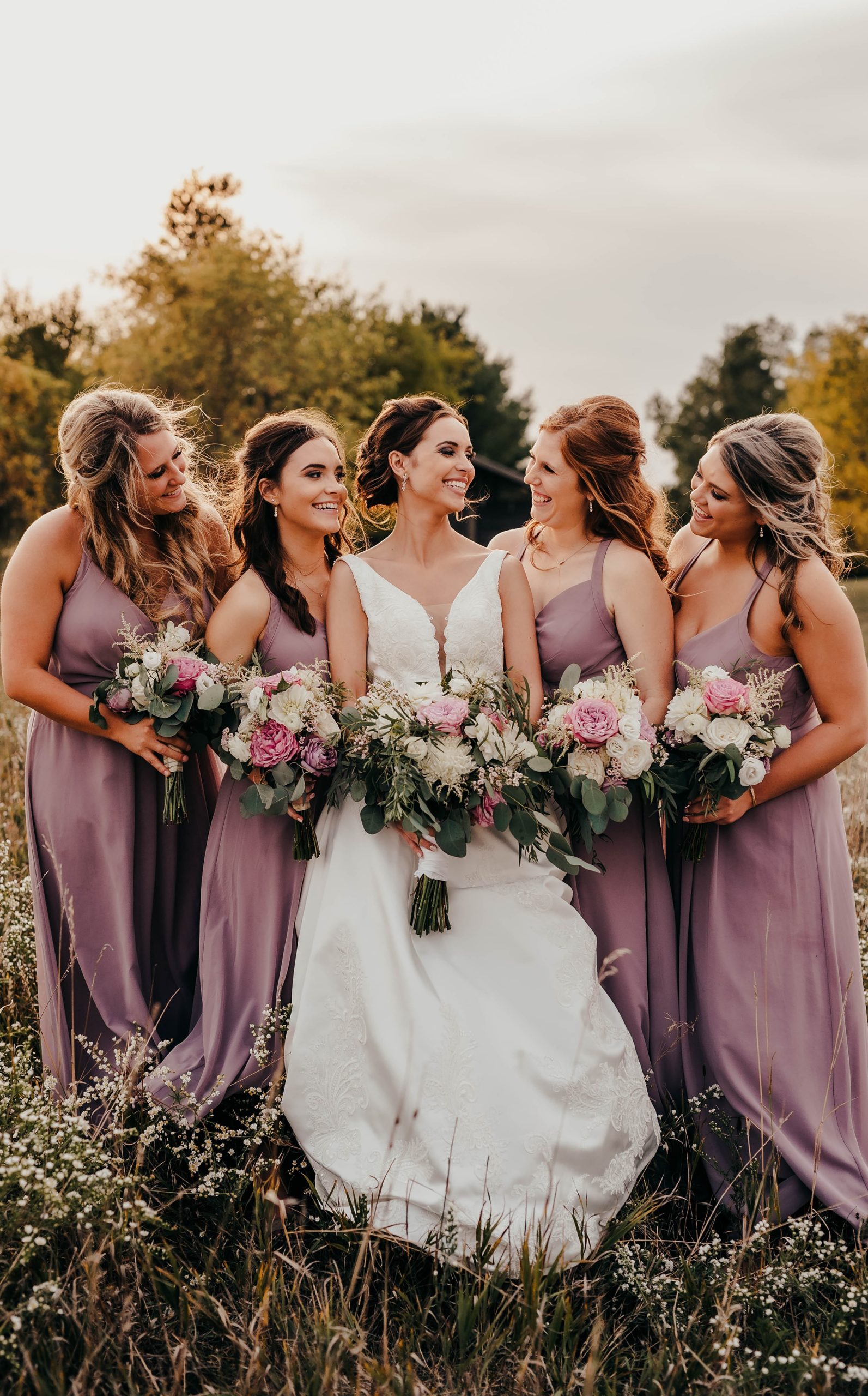 bride and bridesmaids in mauve pose together in field looking at bride