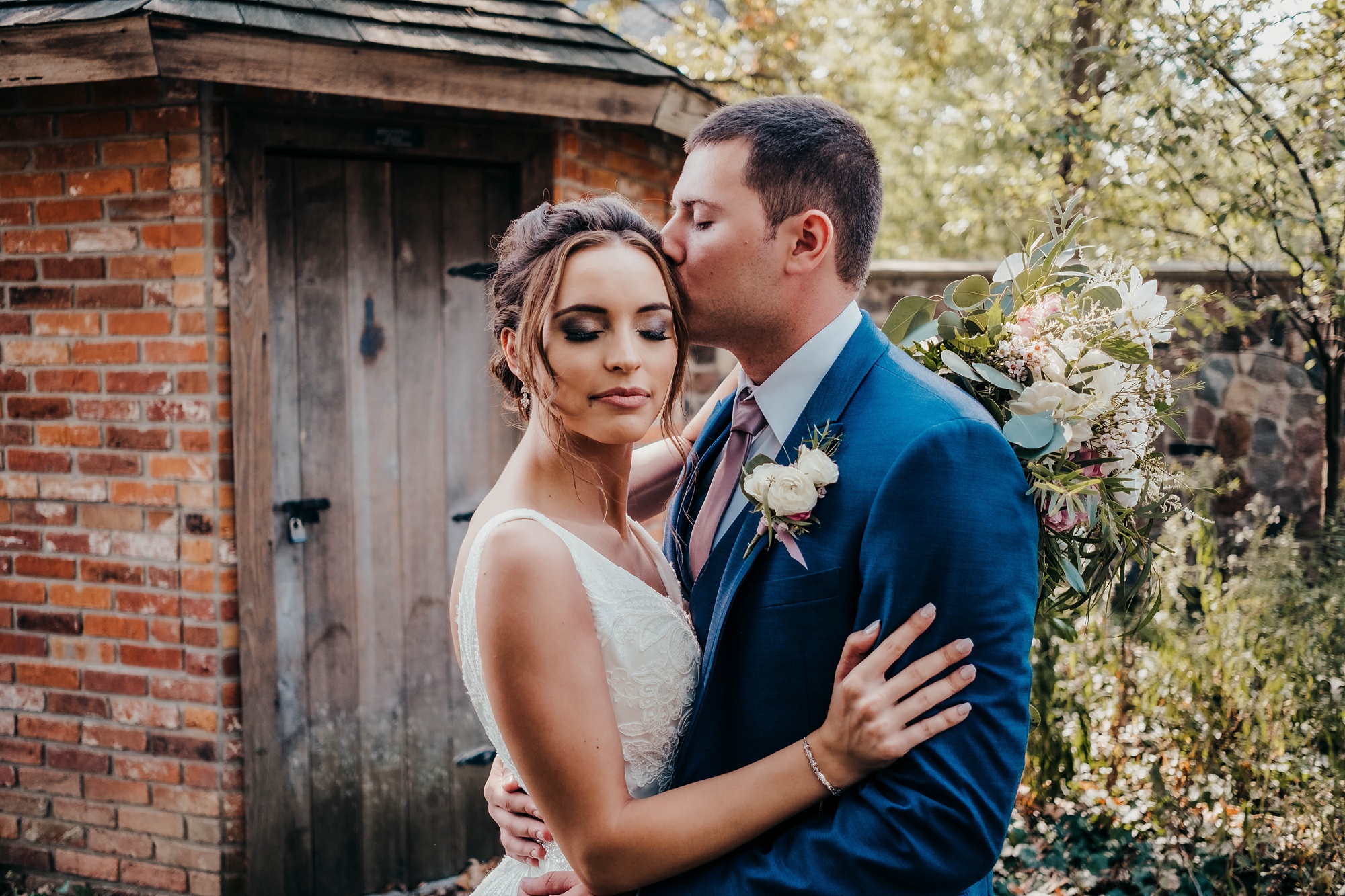 groom kisses bride's forehead during wedding portraits in garden